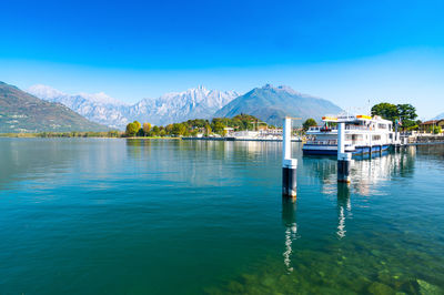 The lakeside of colico, with the mountains, the moored boats, and the small port.