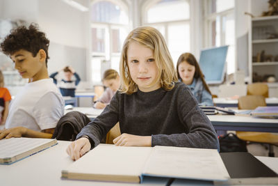 Portrait of schoolboy with blond hair sitting at desk in classroom