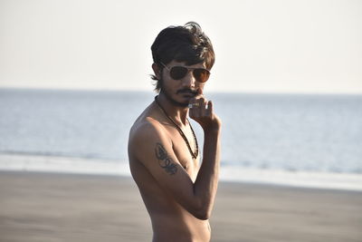 Portrait of shirtless man wearing sunglasses while standing at beach