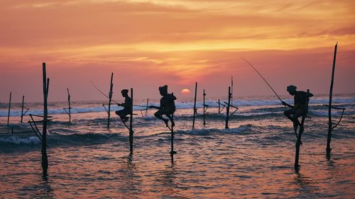 Silhouette people fishing on beach against sky during sunset