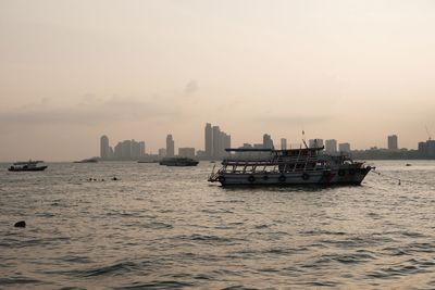 Nautical vessel on sea by buildings against sky during sunset