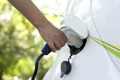 Cropped hand of person charging white electric car