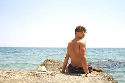 Full length of shirtless man at beach against clear sky