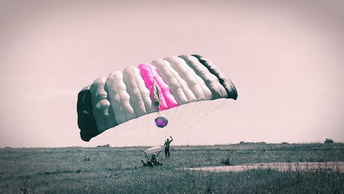 Person paragliding on field against sky