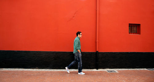 Man standing on footpath against red wall