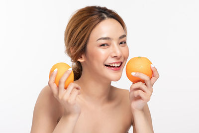 Portrait of a smiling young woman holding apple against white background