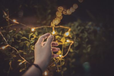 Cropped hand of woman touching illuminated lights at night