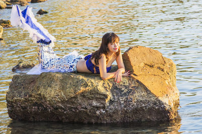 Full length of woman sitting on rock by sea