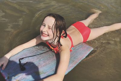 High angle portrait of smiling cute girl on surfboard at beach