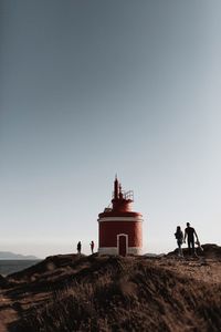 People standing by lighthouse on land against sky