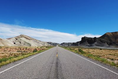 Empty road leading towards mountains against blue sky