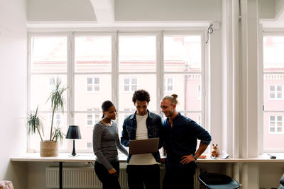 Young businessman holding laptop while discussing with coworkers at workplace