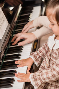 Crop unrecognizable child in checkered dress playing piano while having free time at home on blurred background