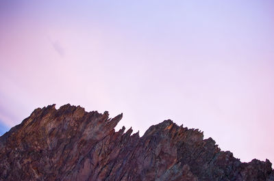 Low angle view of rocky mountain against sky during sunset