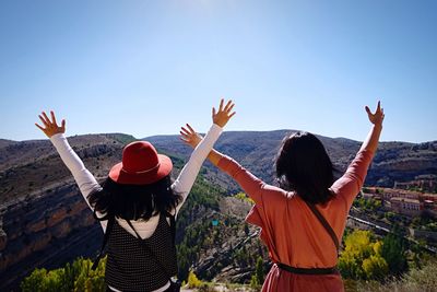 Rear view of friends with arms raised against clear sky