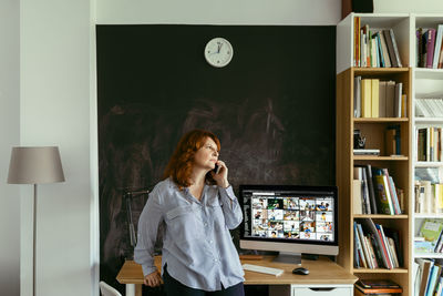 Woman talking on mobile phone while standing by desk at home