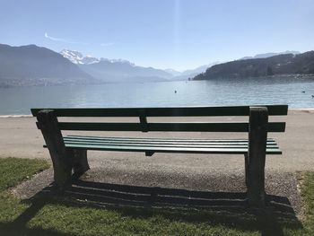 Empty bench by lake against sky