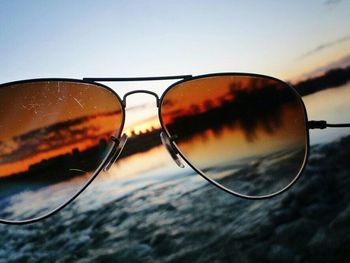 Close-up of sunglasses against sky at sunset