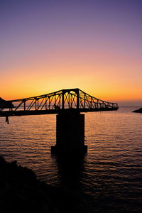 Silhouette of bridge over sea during sunset