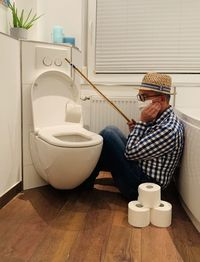  man sitting in bathroom, fishing for toilet paper