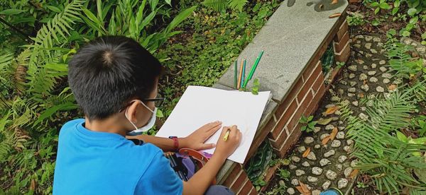 High angle view of boy drawing on book outdoors