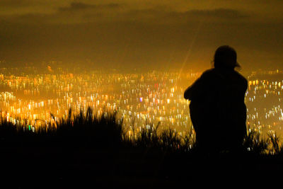 Silhouette man looking at cityscape against sky at night
