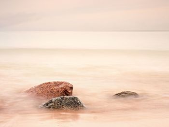 Long exposure of sea and big boulders sticking up. pink sunset at rocky coast of balsitc sea.
