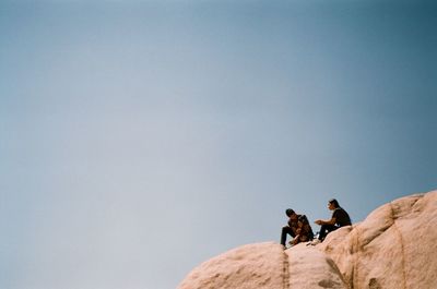 Man photographing woman on rock against sky