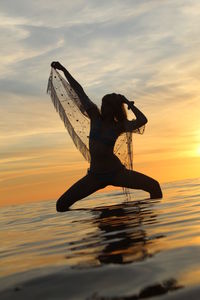 Silhouette woman standing by sea against sky during sunset