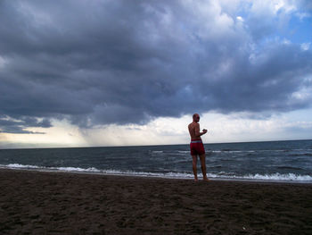 Full length of shirtless man standing at beach against sky