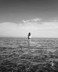 Rear view of woman standing in sea against sky