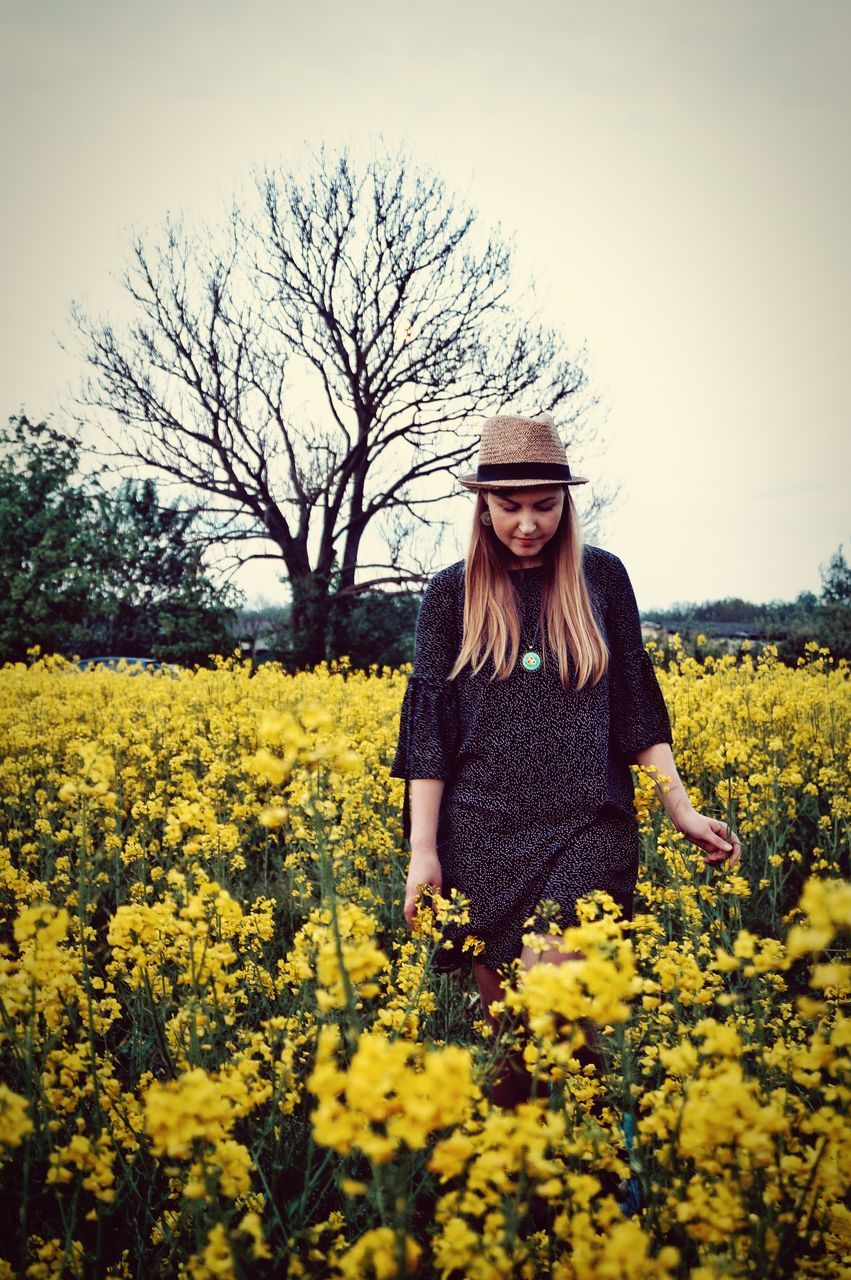 plant, one person, flower, field, flowering plant, yellow, young women, beauty in nature, young adult, growth, sky, land, nature, real people, lifestyles, leisure activity, hair, long hair, casual clothing, front view, hairstyle, beautiful woman, outdoors