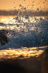 Close-up of wet glass window against sky during sunset