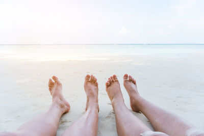 Low section of couple sitting on beach