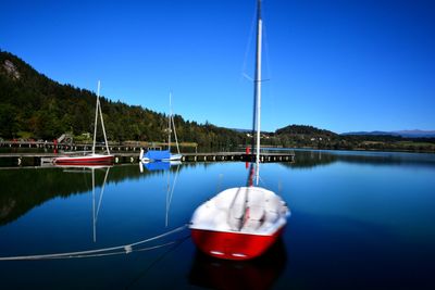 Sailboats moored in lake against blue sky