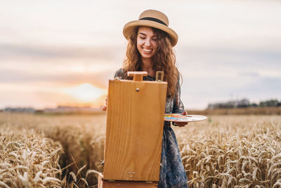 Smiling young woman painting on easel