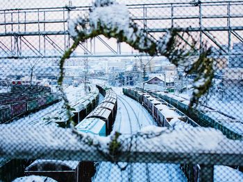 Trains on snow covered field seen through hole in fence
