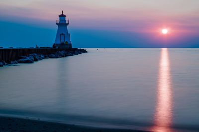 Lighthouse by lake huron against sunset sky