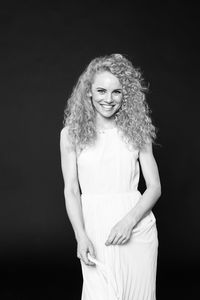 Portrait of smiling woman with curly hair standing against black background