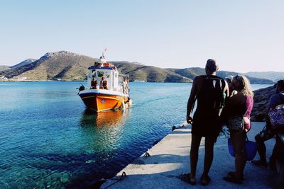 Rear view of people standing on sea against clear sky