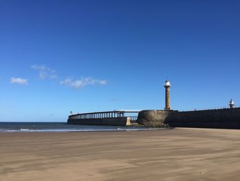 Lighthouse on beach against blue sky