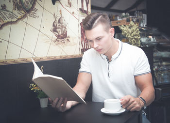 Young man reading book while having drink in cafe