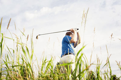 Rear view of man playing golf on field against sky