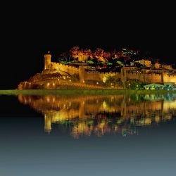 Illuminated city by lake against sky at night