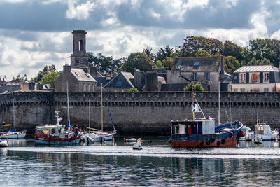 Boats in river by buildings against sky