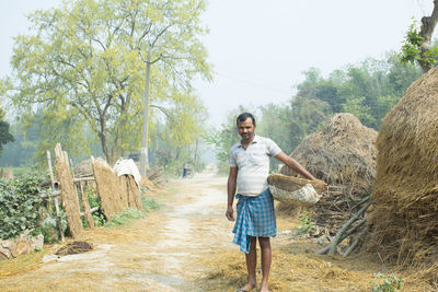 Portrait of young man standing at village holding basket