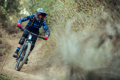 Woman riding on bicycle on path between trees on hill in forest