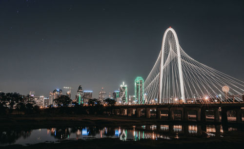 Illuminated bridge over river in city at night