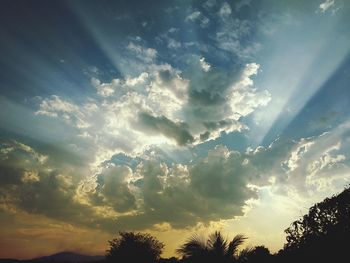 Low angle view of sunlight streaming through clouds