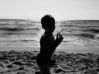 Silhouette shirtless boy gesturing at beach against clear sky